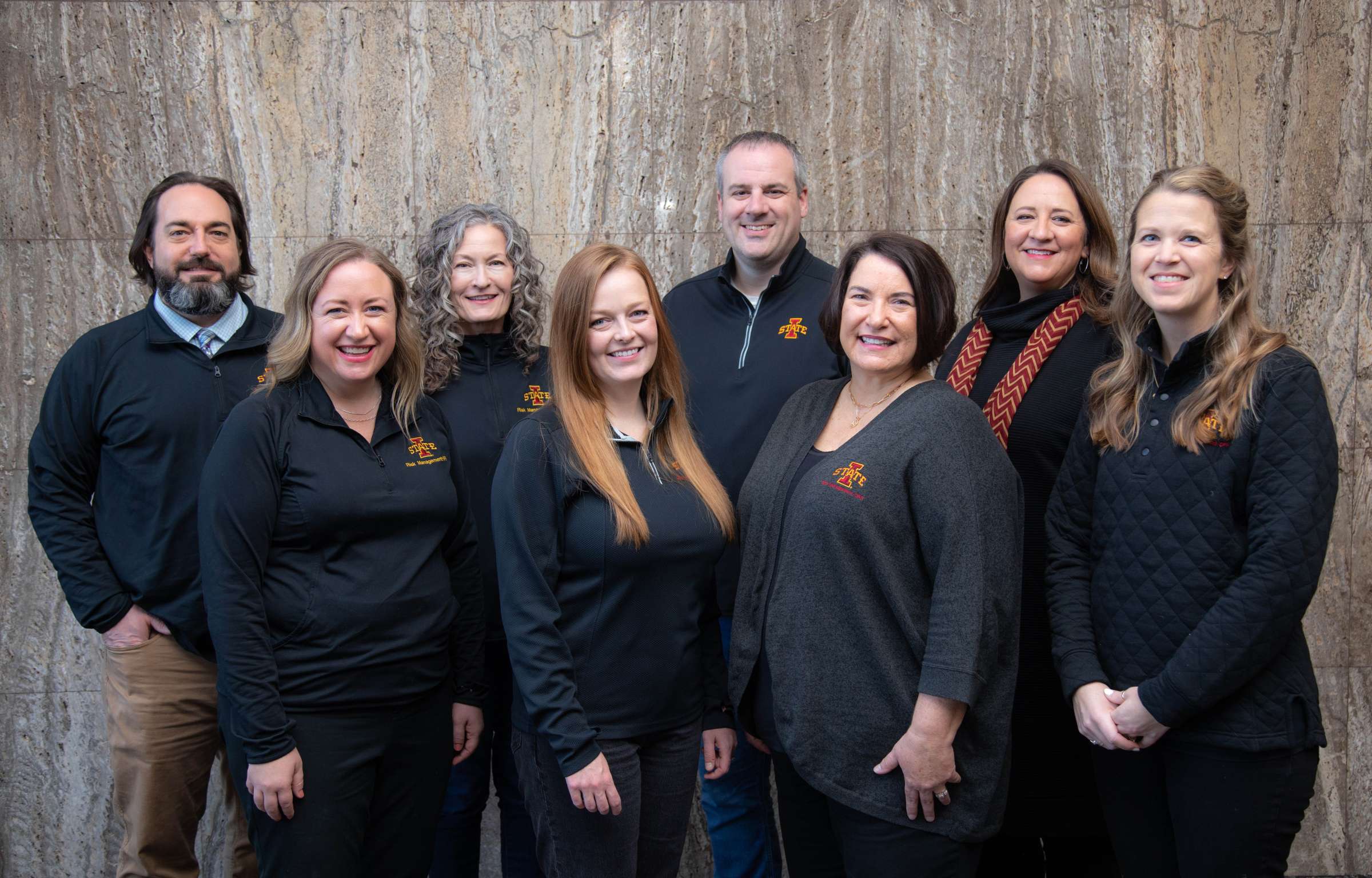 Eight men and women in black Iowa State University attire in front of a marble wall